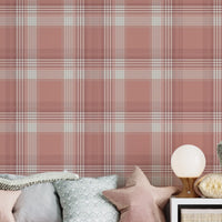 A children's playroom or nursery featuring a dusty terracotta pink and white plaid wallpaper accent wall. A long white storage unit sits against the wall, incorporating cubbies filled with books, storage baskets, and a central built-in bench with a pink velvet cushion and star-shaped pillows. Large plush sea creature toys, including a white octopus, a grey whale, and a blue whale, are scattered across the storage unit and on a yellow textured rug below. The room is finished with light grey wood plank floori