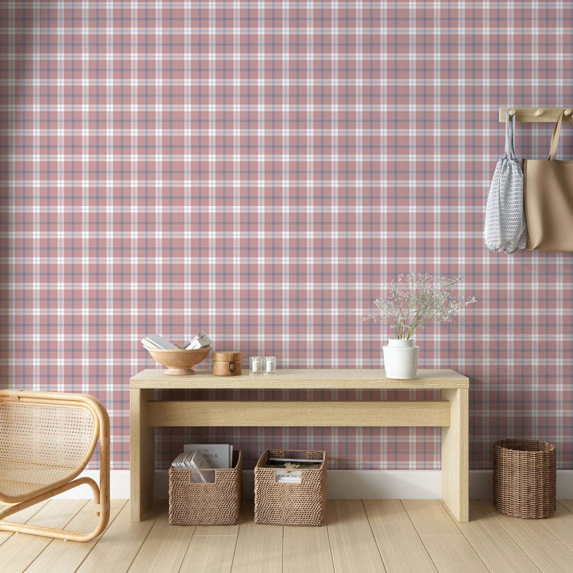A cozy and styled room interior featuring a wall covered in a classic plaid wallpaper with a muted brick red background, crisscrossed with blue, grey, and white stripes. In the foreground, a cream-colored wooden sideboard with woven rattan mesh cabinet doors displays a modern white desk lamp, a small beige ceramic vase, a footed tan bowl sitting on a book, and a small decorative dish with dried botanicals.