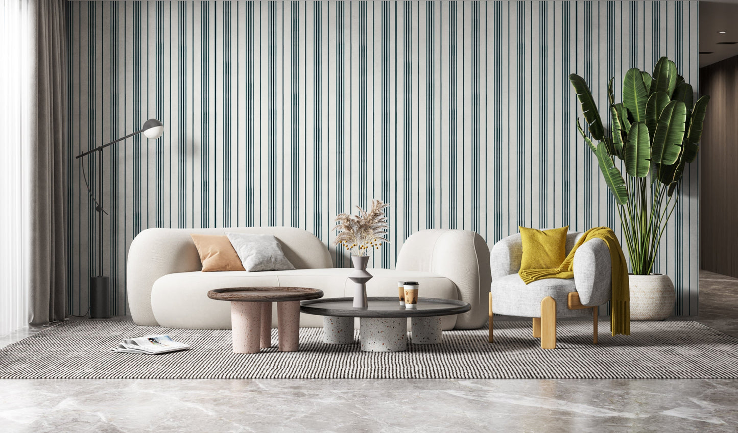 A contemporary living room with a curved white sofa accented by beige and gray throw pillows. Behind the sofa is a white wall with thin vertical teal stripes, while a white vase filled with dried pampas grass and yellow berry stems sits on a table in the foreground.