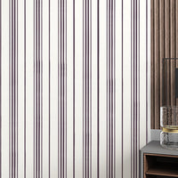 A close-up of a modern interior wall featuring thin vertical plum-colored stripes on a white background. On the right side, part of a contemporary side table displays a textured glass candle holder and a black clock with gold hands against a wood-paneled backdrop.