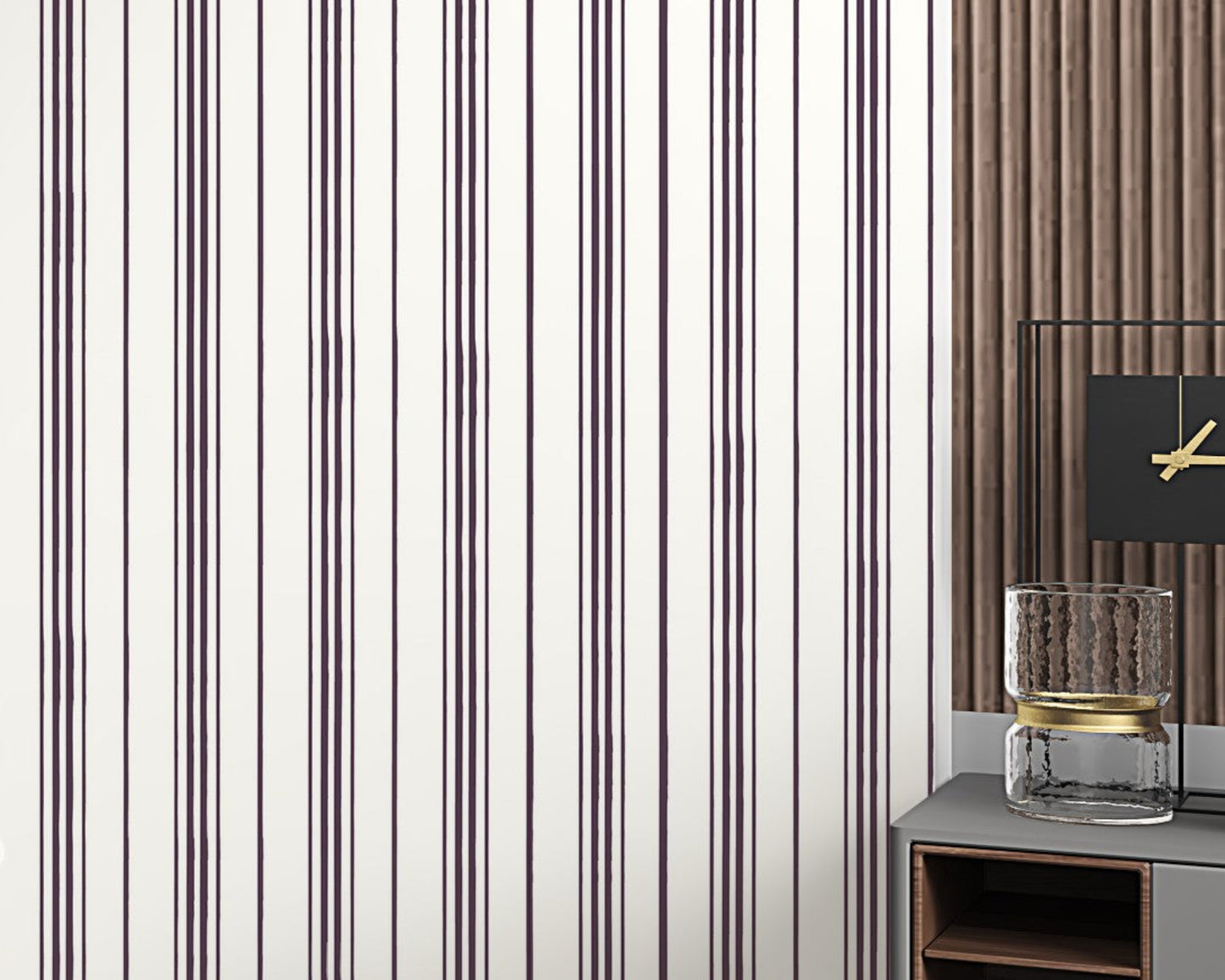 A close-up of a modern interior wall featuring thin vertical plum-colored stripes on a white background. On the right side, part of a contemporary side table displays a textured glass candle holder and a black clock with gold hands against a wood-paneled backdrop.