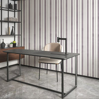 A close-up of a modern interior wall featuring thin vertical plum-colored stripes on a white background. On the right side, part of a contemporary side table displays a textured glass candle holder and a black clock with gold hands against a wood-paneled backdrop.