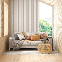 A close-up shot of a beige couch layered with an assortment of textured throw pillows, set against a backdrop of cream-colored wallpaper with vertical brown stripes. The pillows feature various designs, including a grey chunky knit, a white and grey geometric diamond pattern, a smooth brown leather accents, and a bright mustard yellow knit. A fluffy brown faux-fur blanket is also draped over the back of the sofa, creating a warm, cozy interior aesthetic.