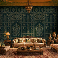 Luxurious living room with traditional Indian-inspired design, featuring intricately carved dark-wood sofas and chairs arranged around a large wooden coffee table on a richly patterned rug. A dramatic teal wall with ornate silver floral and geometric motifs forms the backdrop, illuminated by warm lanterns and an elaborate hanging chandelier. Decorative brass urns, embroidered cushions, and carved architectural details frame the space, while sunlight streams through arched windows.