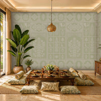 Sunlit tropical dining room with a low wooden table set for a meal on a woven rug, surrounded by floor cushions. Soft sage-green patterned wallpaper covers the walls, while large potted plants, warm brass accents, and a carved pendant light create a relaxed, elegant atmosphere. Floor-to-ceiling glass doors open to a lush palm-filled outdoor view.