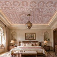 Luxurious traditional bedroom featuring a decorative blush pink ceiling wallpaper with intricate white floral, botanical, and Mughal-inspired motifs arranged in elegant geometric panels. The room showcases carved wooden furniture, a grand upholstered bed dressed in soft cream and blush bedding, matching ornate bedside tables, and a vintage-inspired bench. A large Moroccan-style pendant lantern hangs from the center of the ceiling, while natural sunlight streams through an arched window seat, illuminating th