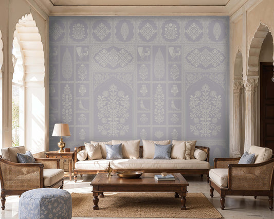 Pastel indigo wallpaper featuring intricate Indian floral motifs, ornamental panels, and traditional decorative elements in soft blue and ivory tones, styled in an elegant living room with wooden cane furniture, neutral upholstery, and arched architectural details.