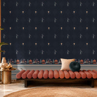 Stylish lounge area featuring a deep navy-blue accent wall decorated with small repeating motifs and an ornate architectural border along the base. The space includes a blush pink upholstered bench with accent cushions, a brass side table with decorative ceramics, and a large potted plant beside an arched window. Warm natural light, soft textures, and rich contrasting colors create an elegant, contemporary interior with Indian-inspired design elements.