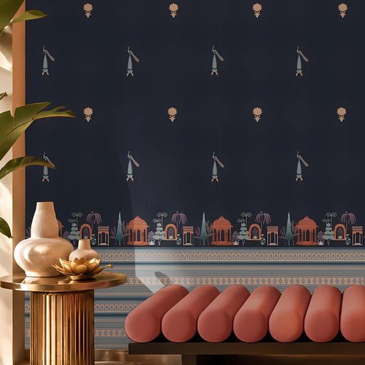 Close-up of a sophisticated interior featuring a deep navy-blue wallpaper with small repeating traditional motifs and an ornate architectural border in muted terracotta and silver tones. In the foreground, a blush pink upholstered bench sits beside a ribbed brass side table topped with ceramic vases and a decorative lotus-shaped object. Soft natural light and tropical greenery create an elegant, contemporary space with Indian-inspired design influences.
