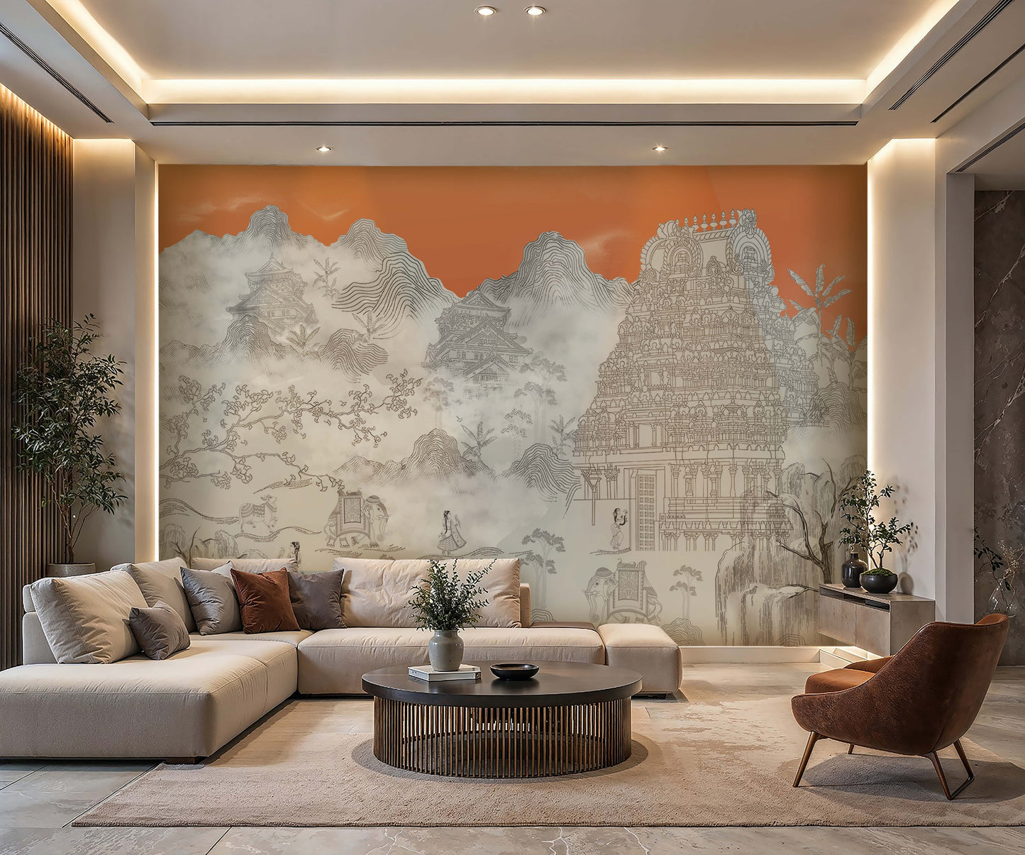 Contemporary living room featuring a large mural wallpaper in soft gray tones depicting misty mountains, traditional architecture, and an ornate South Indian temple against a warm sunset-orange background. The space includes a cream sectional sofa with neutral and rust-colored cushions, a round dark wood coffee table, and a cognac accent chair. Recessed lighting, natural textures, and minimalist furnishings create a serene, sophisticated atmosphere that blends modern design with Asian-inspired artistic elem