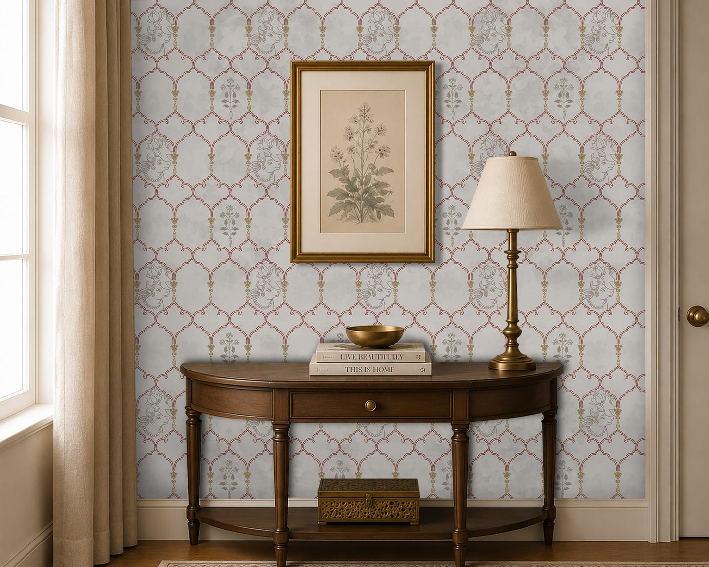 Traditional Indian-inspired wallpaper featuring a delicate trellis pattern with Pichwai-style floral and cow motifs in soft blush and gold tones, displayed in an elegant entryway with a dark wood console table, brass lamp, and framed botanical artwork.
