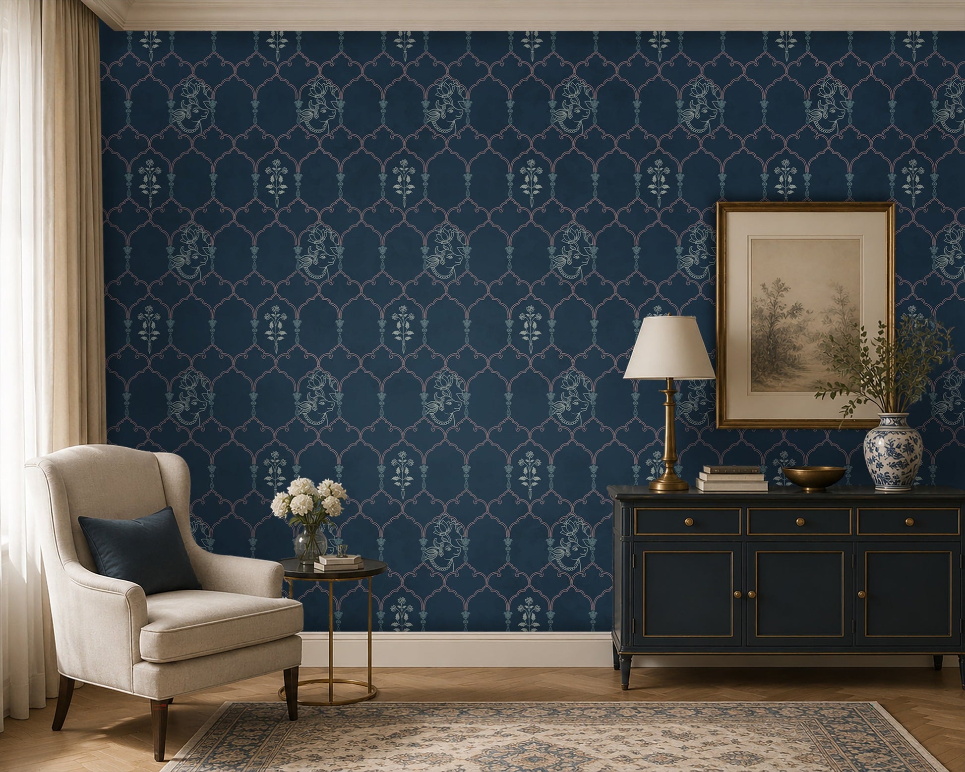Pichwai-inspired wallpaper in deep navy blue featuring an elegant trellis pattern with traditional floral and cow motifs, styled in a sophisticated living room with a cream armchair, dark blue console cabinet, brass lamp, and classic décor accents.
