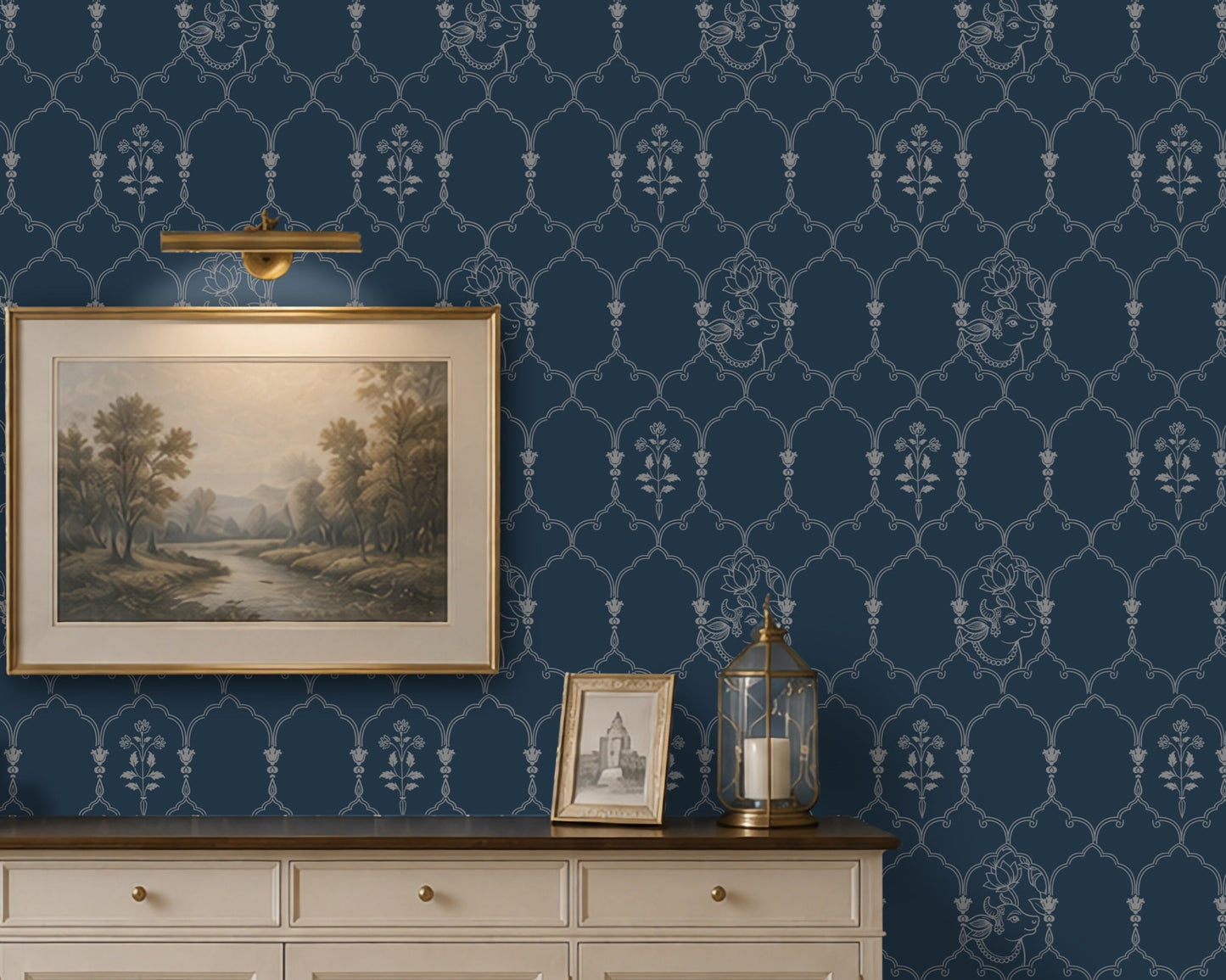 **Alt Text:**
Deep heritage blue wallpaper featuring an intricate Pichwai-inspired trellis pattern with delicate floral motifs and traditional cow illustrations, styled behind a cream sideboard with framed landscape art and brass décor accents in an elegant living room.
