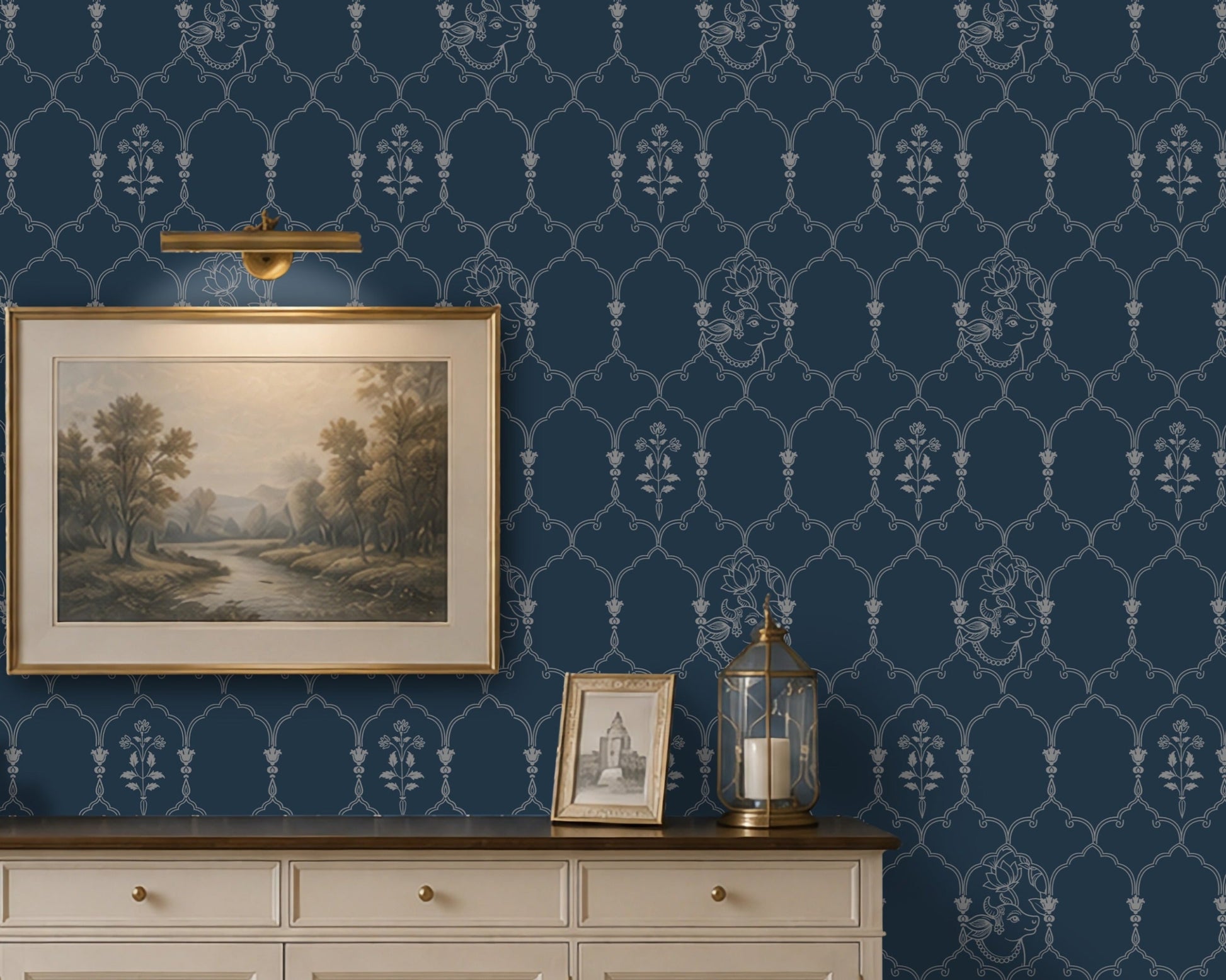 **Alt Text:**
Deep heritage blue wallpaper featuring an intricate Pichwai-inspired trellis pattern with delicate floral motifs and traditional cow illustrations, styled behind a cream sideboard with framed landscape art and brass décor accents in an elegant living room.
