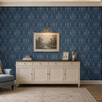 Deep heritage blue wallpaper featuring an intricate Pichwai-inspired trellis pattern with delicate floral motifs and traditional cow illustrations, styled behind a cream sideboard with framed landscape art and brass décor accents in an elegant living room.