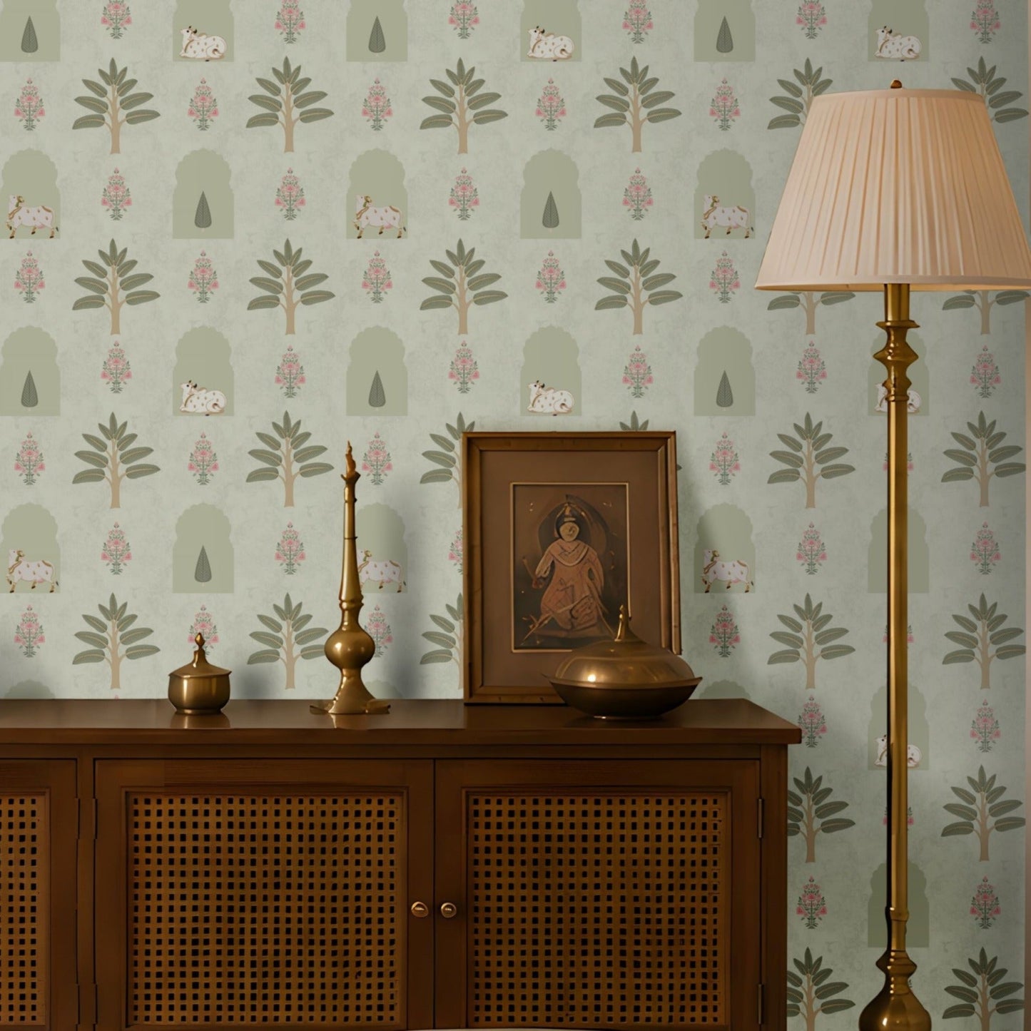 Muted green traditional Indian wallpaper with repeating botanical, arch and cow motifs, paired with wooden furniture and brass accents for a timeless interior.