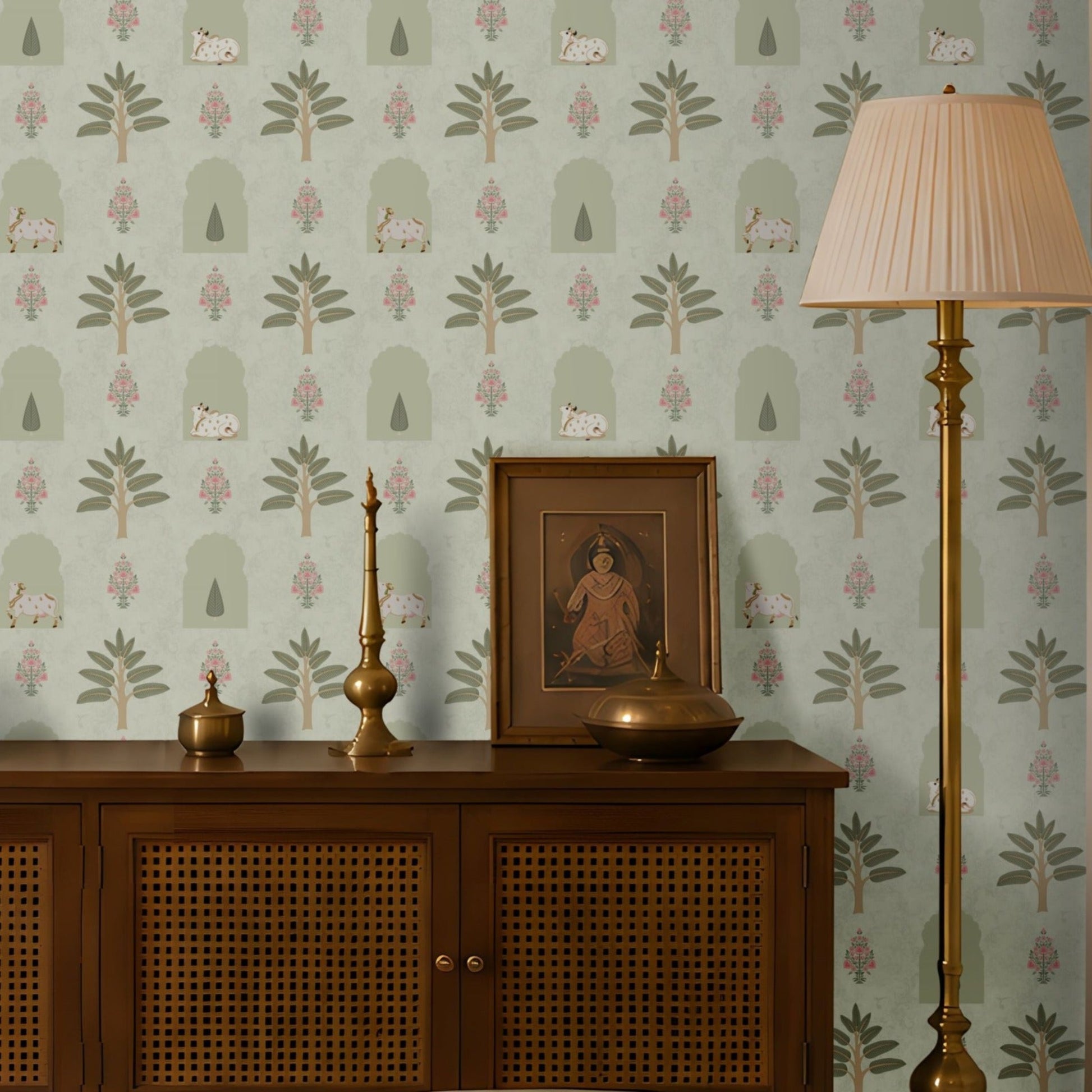 Muted green traditional Indian wallpaper with repeating botanical, arch and cow motifs, paired with wooden furniture and brass accents for a timeless interior.