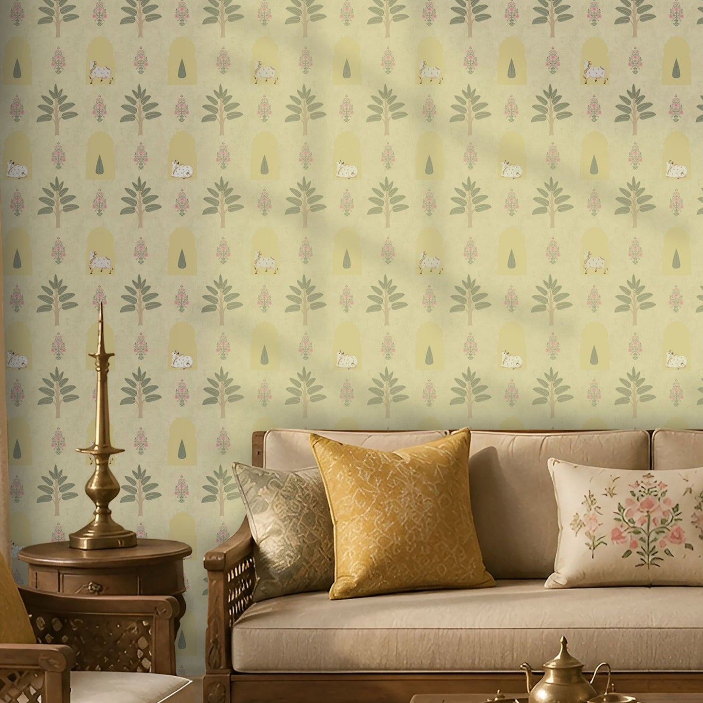 Soft sage Indian heritage wallpaper featuring hand-drawn trees, arches, florals and cow motifs, styled in a warm traditional living room with wooden furniture and brass décor.