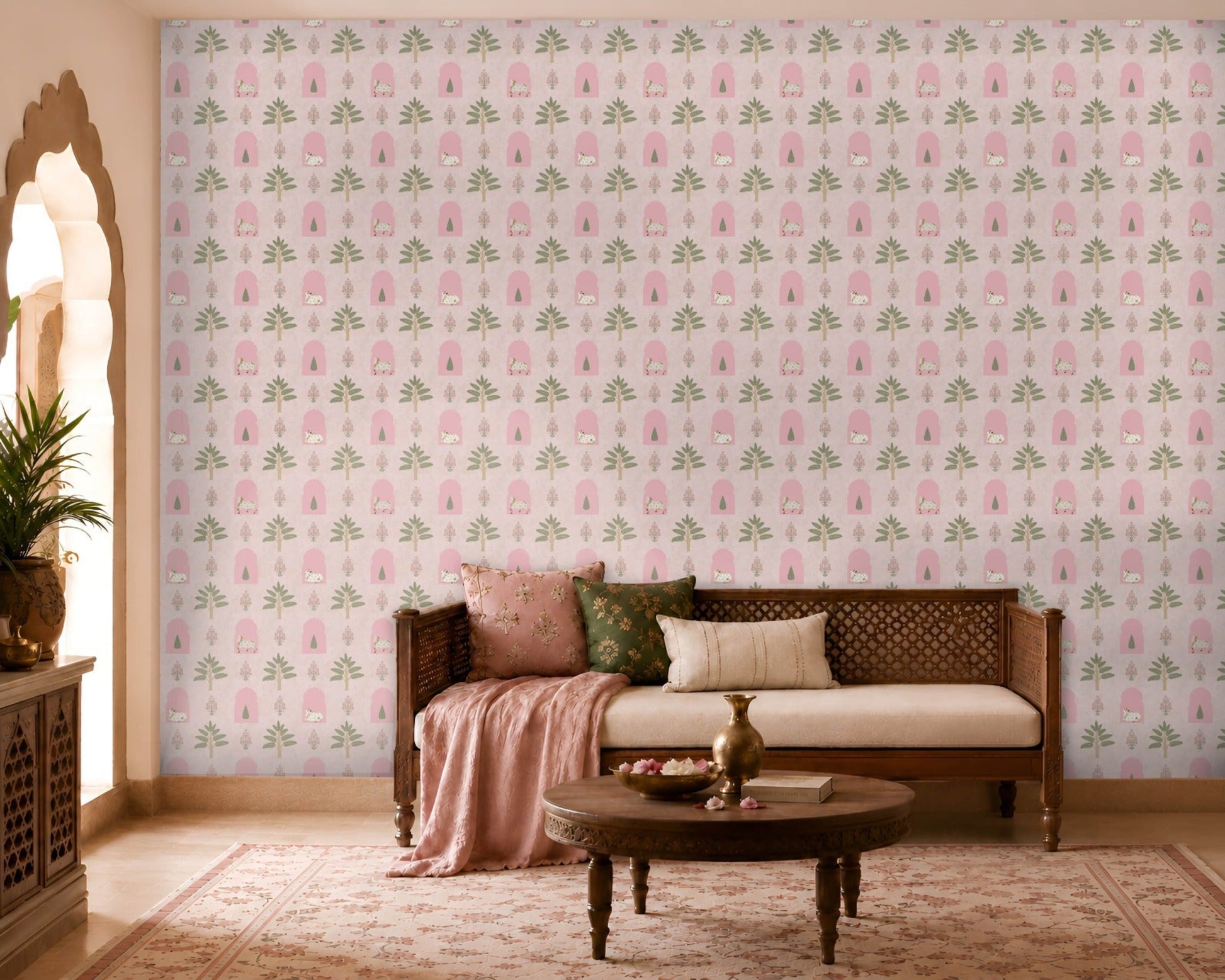 Pink floral wallpaper featuring repeating hand-drawn arches, stylized trees, and delicate botanical motifs, creating a soft Indian-inspired pattern in a warm, elegant living room with wooden furniture and blush-toned décor.