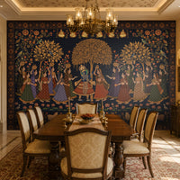 A spacious, elegant dining room with traditional Indian-inspired architecture features a large wooden dining table surrounded by upholstered chairs. The focal point is a striking wall mural depicting Krishna and Radha dancing with attendants beneath ornate trees, framed by intricate floral and geometric patterns in deep blue and gold. Warm lighting from a decorative chandelier, carved archways, antique wooden furniture, a patterned rug, and a sunlit window with cushioned seating 
