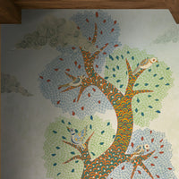 Traditional Gond Art wallpaper mural featuring hand-painted Indian folk art with colorful trees, birds, deer, cattle, and a village woman on a soft ivory background, showcased in a warm contemporary living room with natural wood furniture and earthy décor.