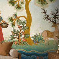 Traditional Gond Art wallpaper mural featuring hand-painted Indian folk art with colorful trees, birds, deer, cattle, and a village woman on a soft ivory background, showcased in a warm contemporary living room with natural wood furniture and earthy décor.