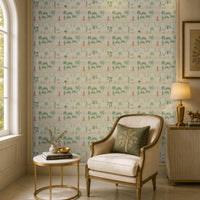 A serene sitting area features a feature wall covered in soft ivory wallpaper with a repeating Mughal-inspired pattern of arches, domed pavilions, palm trees, and figures in traditional attire in muted green and blush tones. In front of the wallpaper, a cream upholstered accent chair with brass trim is paired with a round white-and-gold side table holding a small vase, brass bowl, and stacked books. A ribbed cabinet with a brass table lamp and decorative figurine sits to the side