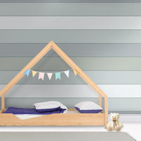 A playful child's bedroom features a modern planked wallpaper in a hit grey theme.
The clean design showcases wide, horizontal shiplap bands in soft shades of grey and muted teal.
In front, a minimalist light-wood house bed frame sits centered on the floor with blue bedding.
The bright, contemporary space is beautifully completed by a small teddy bear sitting on the right.