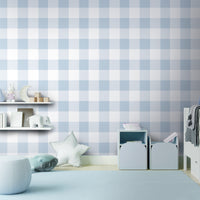 A charming room features a soft pastel checks wallpaper in a frosted blue theme.
The delicate design displays a clean grid pattern with intersecting blue and cream lines.
In front, a small wooden table holds a white vase with small pink flowers.
The sweet, bright interior space creates a calm, simple, and comforting atmosphere.
