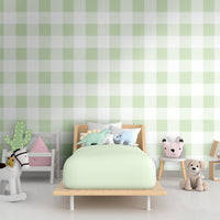 A bright nursery room features a soft gingham check wallpaper in celadon green.
The delicate design displays a large grid pattern with alternating pastel yellow and white blocks.
In front, a white wooden baby crib filled with illustrated animal cushions is centered.
The playful interior space is nicely completed by a tiny white chair holding a soft toy.