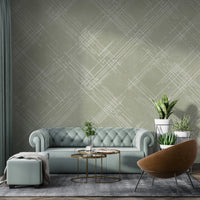 A contemporary living room features a textured crosshatch wallpaper in an olive grey theme.
The fabric-look pattern displays intersecting white sketch lines layered across a muted olive green backdrop.
In front, a comfortable white sofa with grey throw pillows sits behind a round amber glass coffee table.
The calm and stylish interior space is completed by a large leafy green potted plant on the left.