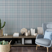 A modern living room features a textured plaid wallpaper in soft lavender grey tones.
The fabric-look pattern displays an intricate grid with intersecting blue-grey and white lines.
In front, a comfortable light blue wingback chair with a matching pillow sits to the right.
The cozy interior space is completed by a low wooden console table holding books and decor.