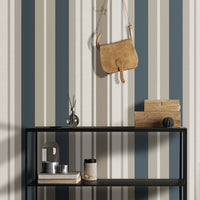 A modern room setup features a bold striped wallpaper in a sagewood theme.
The fabric-textured design shows alternating thick vertical bands of teal blue, warm beige, and soft cream.
In front, a vibrant yellow accent chair with light wood legs stands on the right side.
The contemporary interior setting is completed by a minimalist black metal shelving unit on the left.