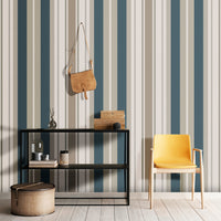 A modern room setup features a bold striped wallpaper in a sagewood theme.
The fabric-textured design shows alternating thick vertical bands of teal blue, warm beige, and soft cream.
In front, a vibrant yellow accent chair with light wood legs stands on the right side.
The contemporary interior setting is completed by a minimalist black metal shelving unit on the left.