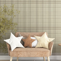 A modern bedroom features a textured plaid wallpaper in sahara blush and cream tones.
The fabric-look design displays a detailed grid pattern with intersecting soft pink, orange, and tan lines.
In front, a fully dressed bed with cream linens sits next to a classic pink wingback accent chair.
The elegant, cozy space is completed by a small wooden nightstand and a soft pink area rug.