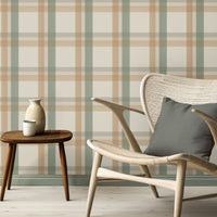 A calm, modern interior space features a classic plaid wallpaper in cream and beige tones.
The detailed fabric-look design displays a structured grid pattern with intersecting tan and sage green lines.
In front, an elegant light wood lounge chair with a dark grey pillow is placed to the right.
The simple minimalist room setting is completed by a small three-legged wooden side table on the left.