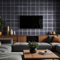 A modern living room features a classic plaid wallpaper in deep charcoal and light grey tones.
The detailed fabric-look design showcases an intricate grid pattern of intersecting lines across the wall.
In front, a unique dark grey tufted accent chair with angled wooden legs is positioned to the right.
The stylish setup is completed by a round white side table holding minimalist vases and decorative items.