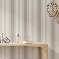 A modern living room features a textured striped wallpaper in a subtle sandstone theme.
The fabric-textured design shows clean vertical lines in light grey, cream, and warm beige.
In front, a minimalist light wooden console table sits straight in the center of the space.
The bright, open interior layout is beautifully completed by a green potted plant on the left.