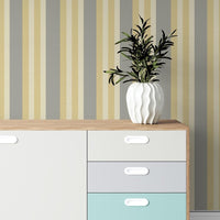 A contemporary room setup features a bold midnight timber wallpaper with vertical stripes.
The textured design displays alternating dark charcoal, brown, and grey vertical bands across the wall.
In front, a rustic wooden desk is paired with a matching wooden chair and a fabric armchair.
The sophisticated interior space is complete with a sleek black desk lamp and an open view window.