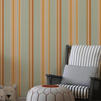 A child's playroom features a muted olive green wallpaper with warm colored stripes.
The detailed pattern shows vertical bands of orange, yellow, and cream running down the wall.
In front, a white giraffe-themed dresser stands next to a dark rocking chair and pouf.
The playful space is neatly arranged with children's toys and a round world map rug.