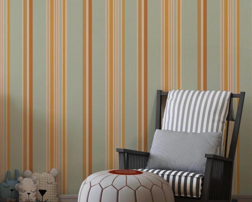 A child's playroom features a muted olive green wallpaper with warm colored stripes.
The detailed pattern shows vertical bands of orange, yellow, and cream running down the wall.
In front, a white giraffe-themed dresser stands next to a dark rocking chair and pouf.
The playful space is neatly arranged with children's toys and a round world map rug.