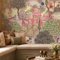 A cozy seating nook with a cushioned bench decorated with patterned pillows in beige, pink, and green. In front sits a small table holding two golden elephant figurines and a vase of white flowers. Behind, a large mural depicts a lush garden with domed pavilions, arches, flowering trees, and figures in traditional attire, creating an elegant and culturally inspired atmosphere.