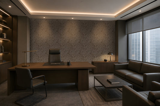 A sophisticated executive office with a warm, contemporary aesthetic: a large walnut desk, dark leather seating, integrated wood cabinetry, a textured taupe-gray feature wall, concealed warm LED lighting, recessed ceiling illumination, floor-to-ceiling windows with roller shades, and a refined lounge area with a leather sofa and marble coffee table. The palette is restrained and architectural, combining dark wood, charcoal, warm gray, and brass accents.
