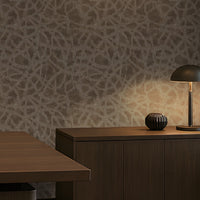 A sophisticated executive office with a warm, contemporary aesthetic: a large walnut desk, dark leather seating, integrated wood cabinetry, a textured taupe-gray feature wall, concealed warm LED lighting, recessed ceiling illumination, floor-to-ceiling windows with roller shades, and a refined lounge area with a leather sofa and marble coffee table. The palette is restrained and architectural, combining dark wood, charcoal, warm gray, and brass accents.
