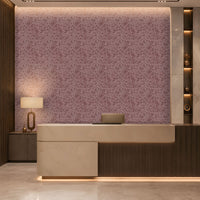 A refined contemporary reception area featuring a large curved-front desk in warm ivory stone and dark wood, with subtle integrated underlighting. The backdrop is a mauve-taupe textured feature wall with an intricate organic pattern and softly illuminated upper edge. Vertical dark-wood slats frame the left side, while marble-clad columns and illuminated display niches with sculptural décor frame the right. Warm architectural lighting, polished stone flooring, and restrained neutral tones create an elegant