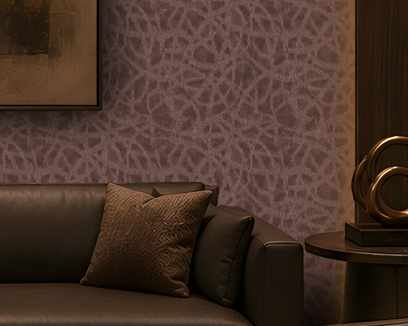 A luxurious contemporary lounge with a symmetrical layout, featuring a dark leather sofa and two matching armchairs around a low rounded rectangular marble coffee table. The room has a warm brown and taupe palette, dark wood built-in shelving, patterned textured wallpaper, brass-accented lighting, sculptural décor, and a large abstract artwork centered on the feature wall. Concealed cove lighting and warm wall sconces create an intimate, sophisticated atmosphere.