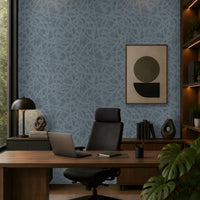 Modern luxury home office featuring dark blue textured wallpaper on the accent wall, a wooden executive desk, black office chair, abstract wall art, built-in wooden shelving, warm ambient lighting, and a large indoor tropical plant