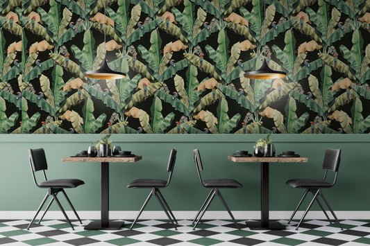 An architectural perspective of a contemporary lounge featuring the Banana Leaves Pattern as a full-scale feature wall. The wallpaper’s lush green and black tones pair strikingly with a cognac leather sectional, gold-toned lighting, and minimalist decor, creating a high-energy and luxurious tropical atmosphere.