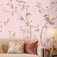 Blush Pink floral wallpaper featuring an elegant botanical design with delicate soft pink blossoms, muted green leaves, graceful winding branches, and subtle ivory floral detailing, creating a sophisticated and seamless visual flow across the feature wall. The wallpaper is showcased in a luxurious contemporary living room with a soft neutral sofa, blush pink velvet accent chairs, decorative cushions, gold-finished side tables, elegant table lamps, a statement crystal chandelier.