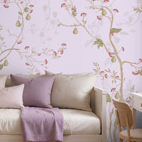 "A serene bedroom with a white daybed topped with purple and cream pillows and a lavender throw blanket. A floral pastel wallpaper covers the wall behind, featuring delicate vines in lavender, green, and pink. To the right, a white desk with a wooden chair, lamp, and vase of flowers sits near a window with Roman shades. Built-in shelves on the left display books and decorative items. Soft natural light and a ceiling lamp create a calm, elegant atmosphere."